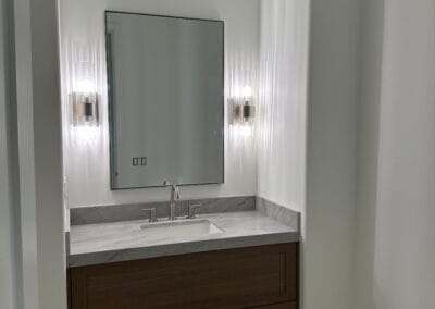 Bathroom remodel featuring custom lighting fixtures, gray stone countertops, and dark wood, minimalistic modern cabinets.