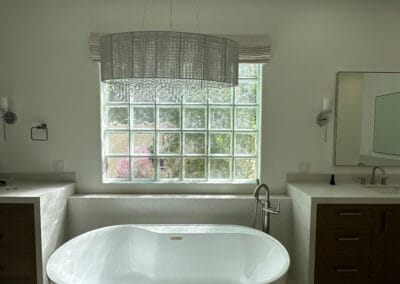 Elegant and modern master bathroom remodel with big white freestanding tub. Gorgeous white stone backsplash and chrome faucet. Elegant Chandelier hangs above the tub.