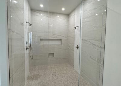 beautifully remodeled double shower features custom stone walls and shower floors with elegant modern glass design.