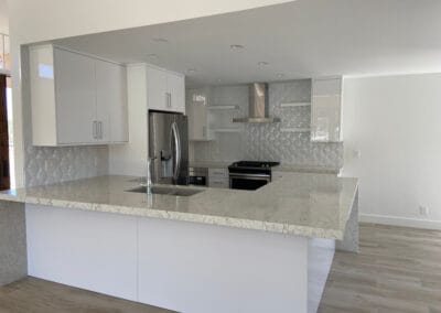 A beautiful designer style kitchen is featured with elegant marble stone countertops and custom backsplash. Minimalist, modern, white cabinets.