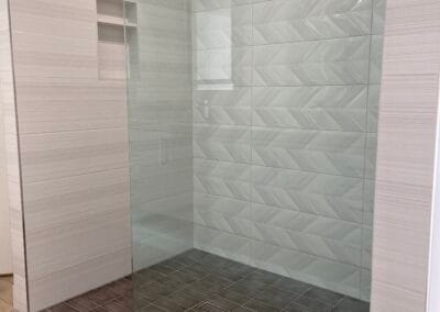 Custom rainfall style shower renovation with dark floor stone tile and white wall tile, open shower with glass.