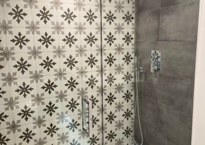 Elegant shower renovation featuring custom wall tile with spoke pattern adjacent gray stone tile and overhead showerhead.