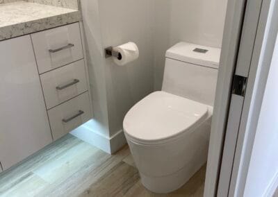 Image features an upgraded bathroom remodel with toilet, flooring, countertop, and lighting upgrades