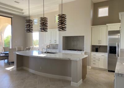 Home interior remodel features an elegant and modern kitchen design with designer lighting, white cabinets, and upgraded countertops and island in open space.