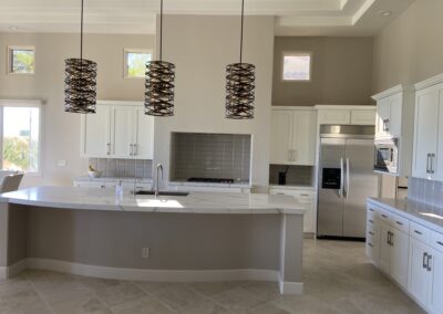 Home interior remodel features an elegant and modern kitchen design with designer lighting, white cabinets, and upgraded countertops and island in open space.