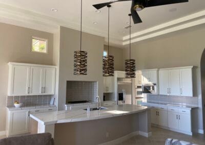 Home interior remodel features an elegant and modern kitchen design with designer lighting, white cabinets, and upgraded countertops and island in open space. A designer ceiling fan is featured.