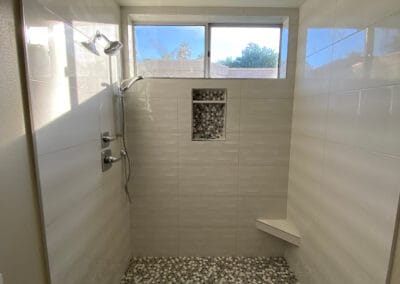 Beautiful, remodeled shower with white stone tile walls and black, white, gray hexagon floor tile.