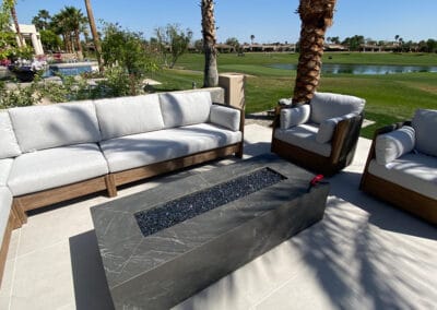 Modern firepit and patio with white and wooden furniture sits on a country club golf course featured in the background.