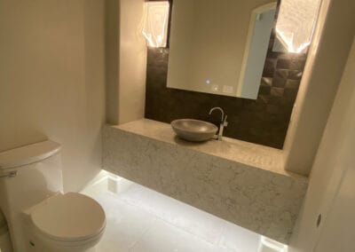 Custom lighting featured in brilliant custom home bathroom remodel. Designer mirror with modern stink and stone countertop and large tile flooring.