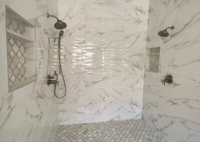 Custom overhead shower remodel with three showerheads. Beautiful white stone walls with diamond stone flooring.