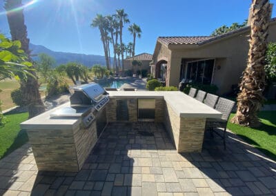 Upgraded custom BBQ with countertop with chairs for guests. Overlooks a country club golf course. A house sits in the background.