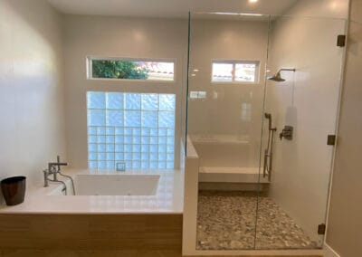 modern design bathroom remodel featuring tile shower with gray and white flooring. A big square custom bathtub with light wood patterned flooring.