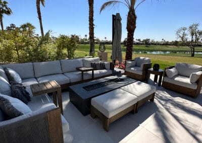 Modern firepit and patio with white and wooden furniture sits on a country club golf course featured in the background.