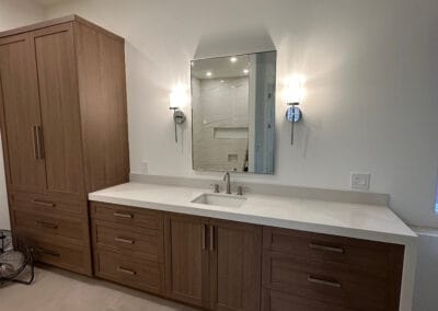 Sleek modern design bathroom remodel featuring white countertops, dark wood cabinets and custom lighting. Stone flooring.