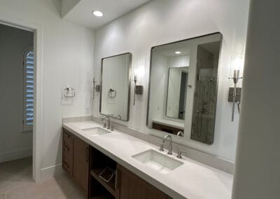 Home remodel bathroom renovation featuring rounded square mirrors and sinks. White countertops against modern dark wood cabinets.