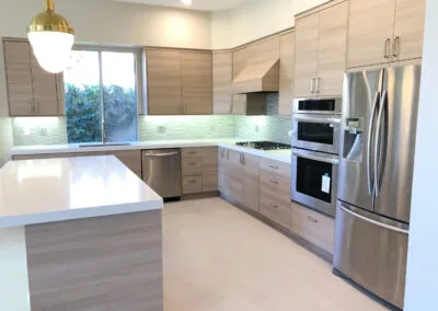 Home interior remodel features an elegant and modern kitchen design with stylish lighting, wooden finish cabinets, and upgraded countertops, island, and backsplash.