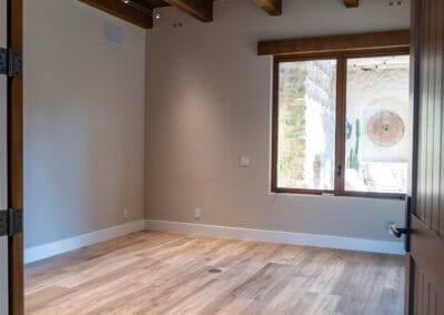 Gorgeous home remodel featuring bedroom with wood floors, and custom ceiling fan. Wood trim accent above window and custom lighting with ceiling rafters exposed.